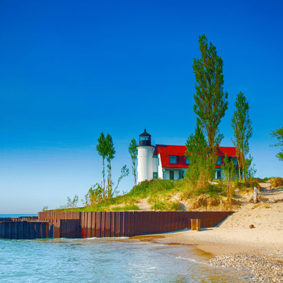 Lighthouse rests on the Lake Michigan Shoreline with blue skies in background and sandy beach.